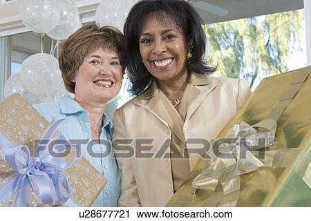 Stock Image - Two middle-aged women holding gifts at party. Fotosearch
