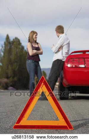 Stock Photo - Two motorists standing by broken down car with warning triangle behind it. Fotosearch