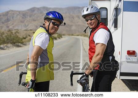 Stock Image - Two Senior men with bikes on road. Fotosearch