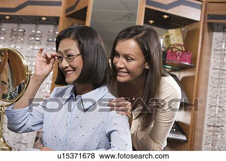 Stock Photo - Two women trying on eyeglasses in store. Fotosearch