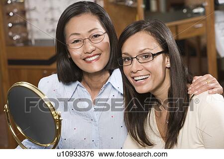 Stock Photograph - Two women trying on eyeglasses in store. Fotosearch