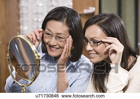 Stock Photograph - Two women trying on eyeglasses in store. Fotosearch