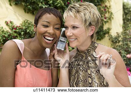 Two women using mobile phone outdoors View Large Photo Image Stock Image - Two women using mobile phone outdoors. Fotosearch