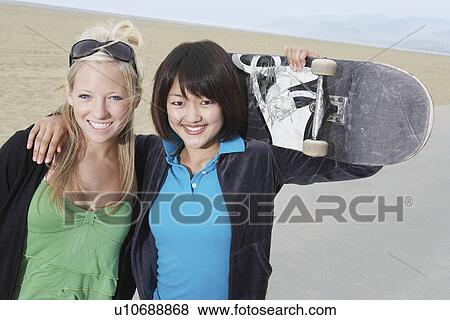 Stock Photo - Two young female skateboarders on beach, portrait. Fotosearch
