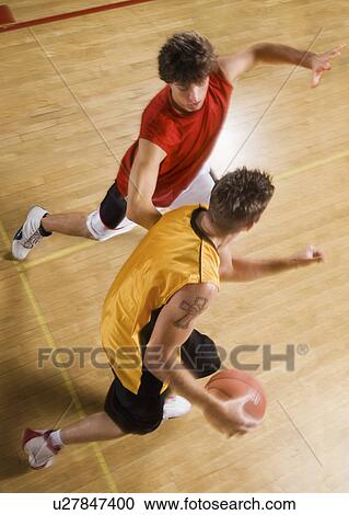 Stock Image - Two young men playing basketball on indoor court. Fotosearch