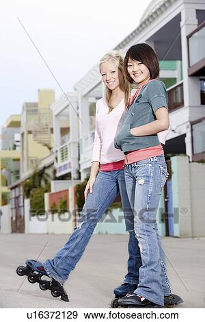 Stock Photo - Two young woman wearing rollerblades on city street. Fotosearch