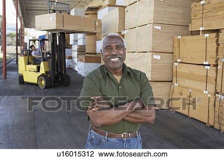 Stock Image - Warehouse Worker in front of man working with forklift. Fotosearch