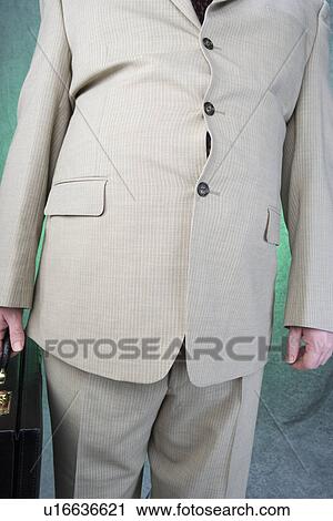Stock Image - Well-dressed overweight mid-adult man standing and holding briefcase, mid section. Fotosearch