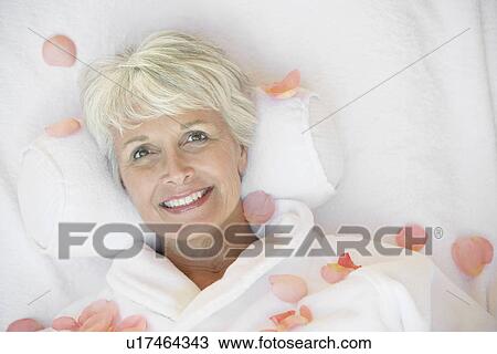 Stock Image - Woman at spa with rose petals around, head and shoulders. Fotosearch