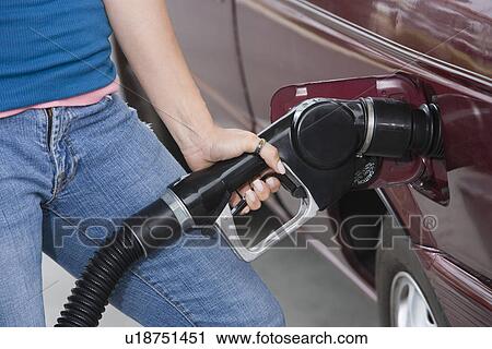 Stock Image - Woman by car with fuel pump, mid section. Fotosearch