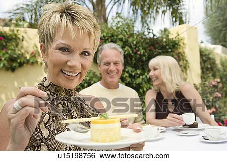 Stock Photograph - Woman eating dessert with friends outdoors. Fotosearch