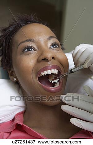 Stock Photo - Woman having teeth examined at dentists, (close-up). Fotosearch