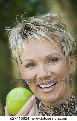 Picture - Woman holding apple outdoors, portrait. Fotosearch