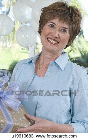 Stock Image - Woman holding gift at party. Fotosearch