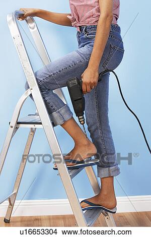 Picture - Woman holding power drill on stepladder, low section. Fotosearch