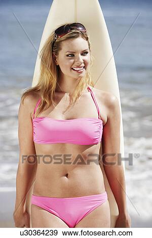 Stock Photo - Woman leaning on surfboard on beach. Fotosearch