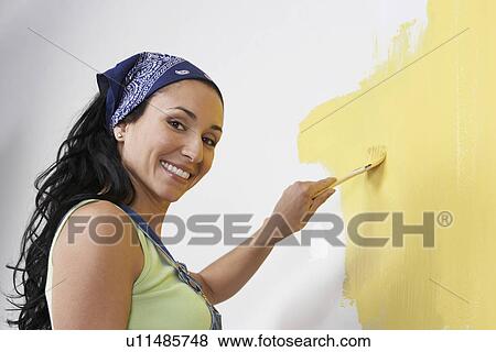 Stock Photo - Woman painting interior wall, low-angle view, portrait. Fotosearch