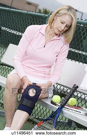 Stock Image - Woman putting on knee band. Fotosearch