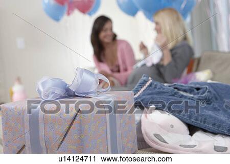 Stock Image - Woman sitting behind gifts at baby shower, focus on foreground. Fotosearch