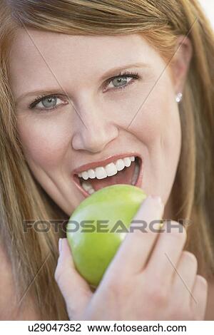 Stock Image - Woman taking bite out of apple, portrait, (close-up), (portrait). Fotosearch