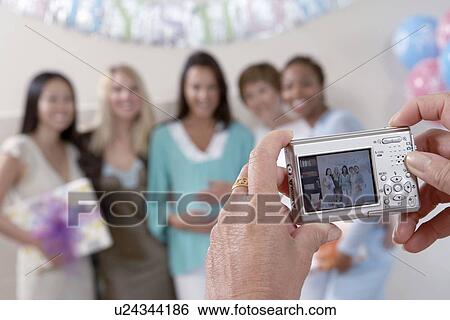 Stock Photograph - Woman taking photo of friends at baby shower, focus on camera. Fotosearch
