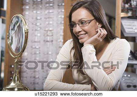Stock Image - Woman trying on eyeglasses in store. Fotosearch