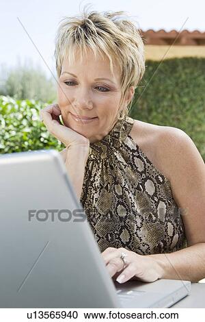 Stock Image - Woman using laptop in back yard. Fotosearch