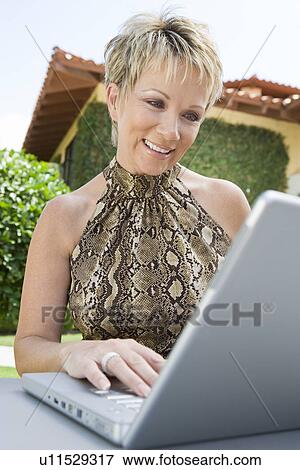 Woman using laptop in back yard View Large Photo Image Stock Photo - Woman using laptop in back yard. Fotosearch