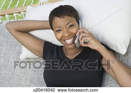 Stock Image - Woman using mobile phone in hammock, portrait. Fotosearch