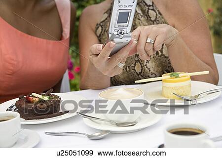 Stock Photo - Women using mobile phone by dessert on table. Fotosearch