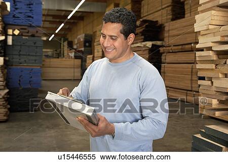 Stock Photography - Worker checking clipboard in warehouse of wood. Fotosearch