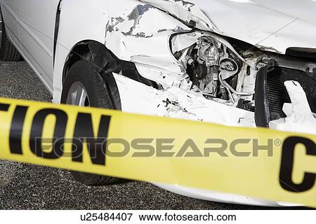 Stock Photo - Wrecked car behind warning tape, close up. Fotosearch