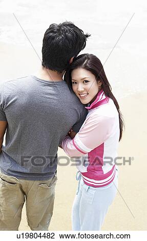 Stock Image - Young couple arm in arm on beach, elevated view. Fotosearch