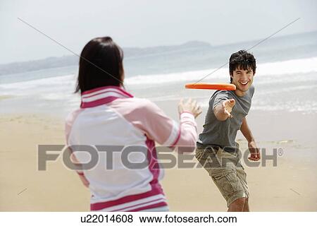 Stock Photo - Young couple playing Frisbee on Beach. Fotosearch