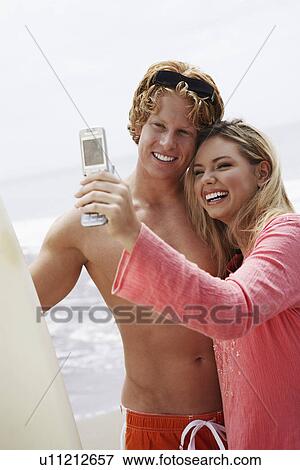 Stock Photo - Young couple taking picture with cell phone on beach. Fotosearch