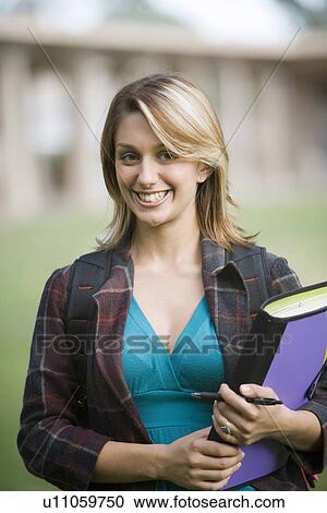 Stock Image - Young female student holding a book and looking at camera. Fotosearch