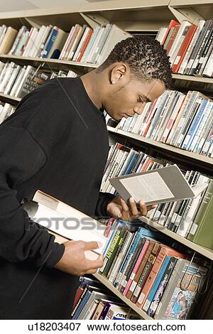 Stock Photo - Young man choosing books in library. Fotosearch