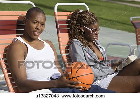 Stock Image - Young Man Holding Basketball, Relaxing with Friend, Portrait. Fotosearch