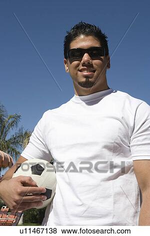 Stock Photo - Young man holding soccer ball outdoors, portrait. Fotosearch