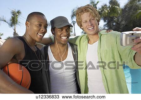 Stock Image - Young man photographing self and two friends. Fotosearch