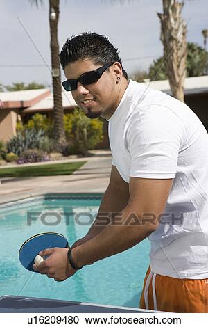 Stock Image - Young Man Playing Ping-Pong by Swimming Pool. Fotosearch