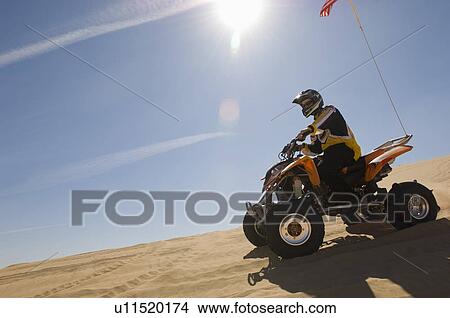 Picture - Young Man Riding ATV Over Sand Dune. Fotosearch