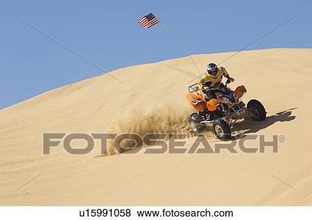 Stock Photo - Young Man Riding ATV Over Sand Dune. Fotosearch