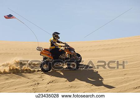 Stock Photo - Young Man Riding ATV Over Sand Dune. Fotosearch
