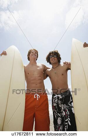 Stock Image - Young men holding surfboards, low angle view. Fotosearch
