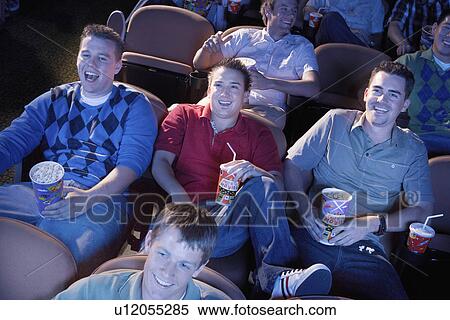 Stock Photography - Young men reclining, watching movie in theatre, smiling. Fotosearch