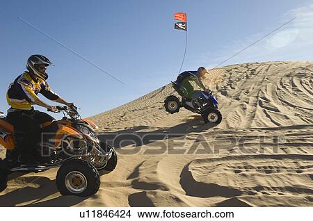 Picture - Young Men Riding ATVs Over Sand Dunes. Fotosearch