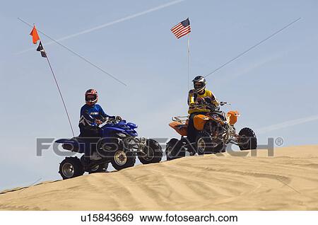 Stock Photo - Young Men Riding ATVs Over Sand Dunes. Fotosearch