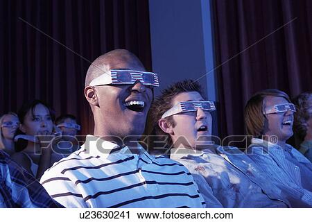 Stock Image - Young men wearing 3-d glasses watching 3-D movie in theatre. Fotosearch