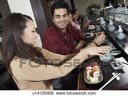 Stock Photography - Young people eating sushi with chopsticks in restaurant. Fotosearch